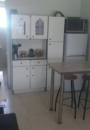 Una cocina con armarios blancos, un refrigerador, un microondas y una mesa con taburetes.