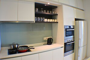 A kitchen with white cabinets, a built-in oven, a coffee maker, and a red frying pan on the counter. - Skyline Service Suite KLCC at Platinum (Kuala Lumpur)