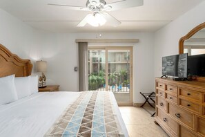 Habitación de hotel con cama, cómoda, televisor y balcón con vistas al exterior.