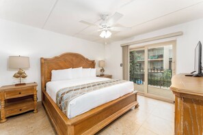 A hotel room with a wooden bed, two bedside tables with lamps, a ceiling fan, and a view of the outside balcony. - Beach View 214 - Easy Beach Access Family Condo (South Padre Island)