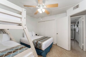 Un dormitorio con literas, ventilador de techo, puerta que da al baño y edredón estampado.