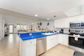 A modern kitchen with white cabinets, a blue countertop, and stainless steel appliances including a microwave and dishwasher. - Beach View 214 - Easy Beach Access Family Condo (South Padre Island)