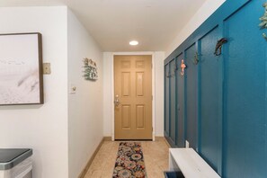A hallway with a wooden door, a wall-mounted light fixture, and a patterned rug. - Beach View 214 - Easy Beach Access Family Condo (South Padre Island)