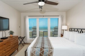 A hotel room with a bed, a TV, a dresser, a plant, and a balcony with chairs. - Seville 405 - Beachfront Condo Private Balcony, 2 Pools (South Padre Island)