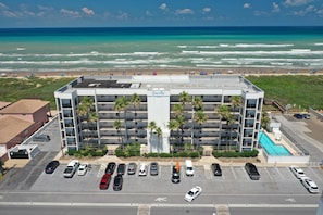 Ein mehrstöckiges Hotel mit Pool, Parkplatz und Blick auf Strand und Meer.