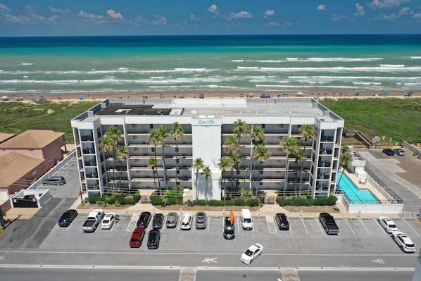 A multi-story hotel with a pool, parking lot, and a view of the beach and ocean. - Seville 405 - Beachfront Condo Private Balcony, 2 Pools (South Padre Island)