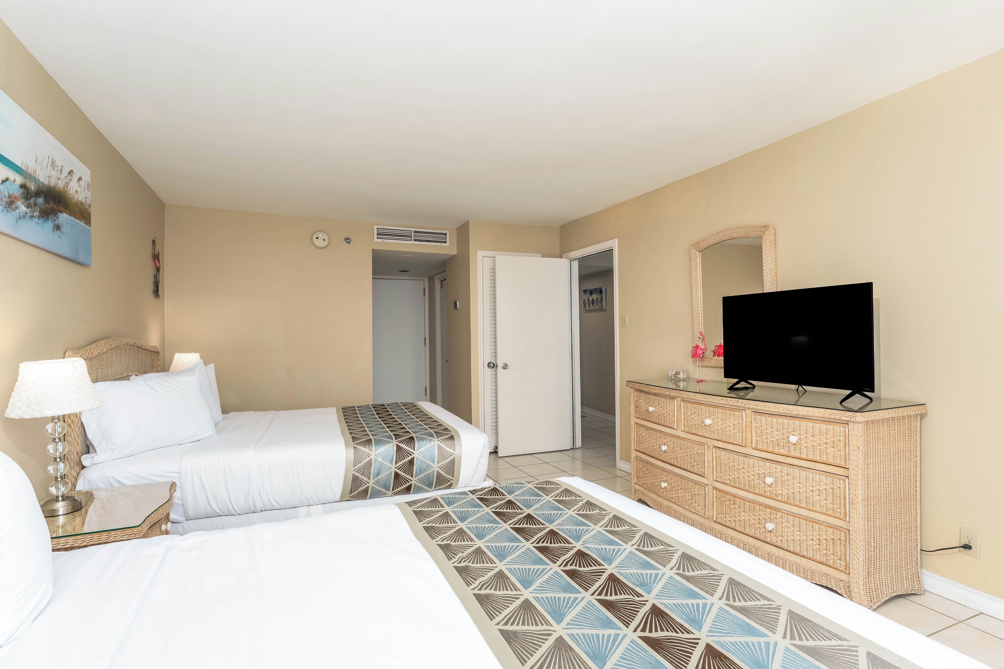 A hotel room with two beds, a television, a dresser, and a painting on the wall.