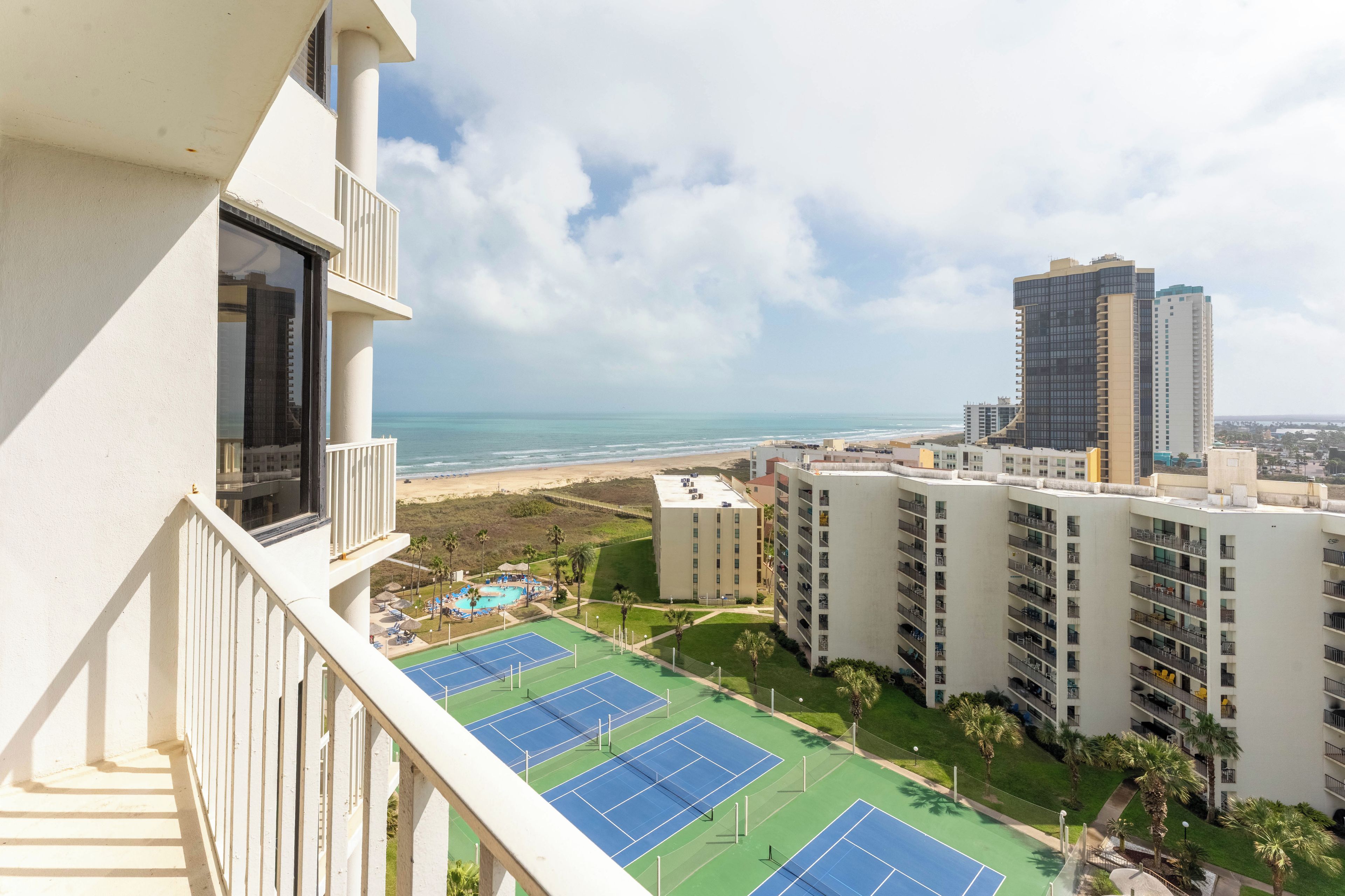 A high-rise hotel with a tennis court and a beach view.