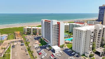 A high-rise hotel with multiple floors, a parking lot, and a view of the beach.