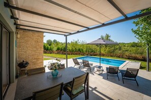 Um pátio externo com piscina, área de estar coberta e mesa com cadeiras.