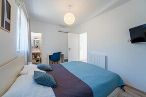 Quarto com cama, escrivaninha, cadeira e televisão.
