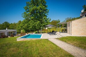 Ein Garten mit Pool, überdachter Terrasse und einem Steinhaus.