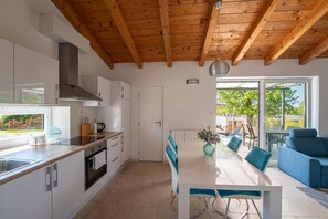 Eine moderne Küche mit Holzbalken, einem Essbereich mit Tisch und Stühlen sowie Blick durch eine Glastür.
