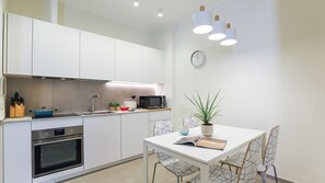 A modern kitchen with white cabinetry, a built-in oven, a microwave, and a dining table with chairs. - Italianway Comfort - Soperga 15 (Milan)