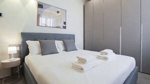 A neatly made bed with white linens and folded towels, a bedside lamp, and a large mirror above the bed. - Italianway Comfort - Soperga 15 (Milan)