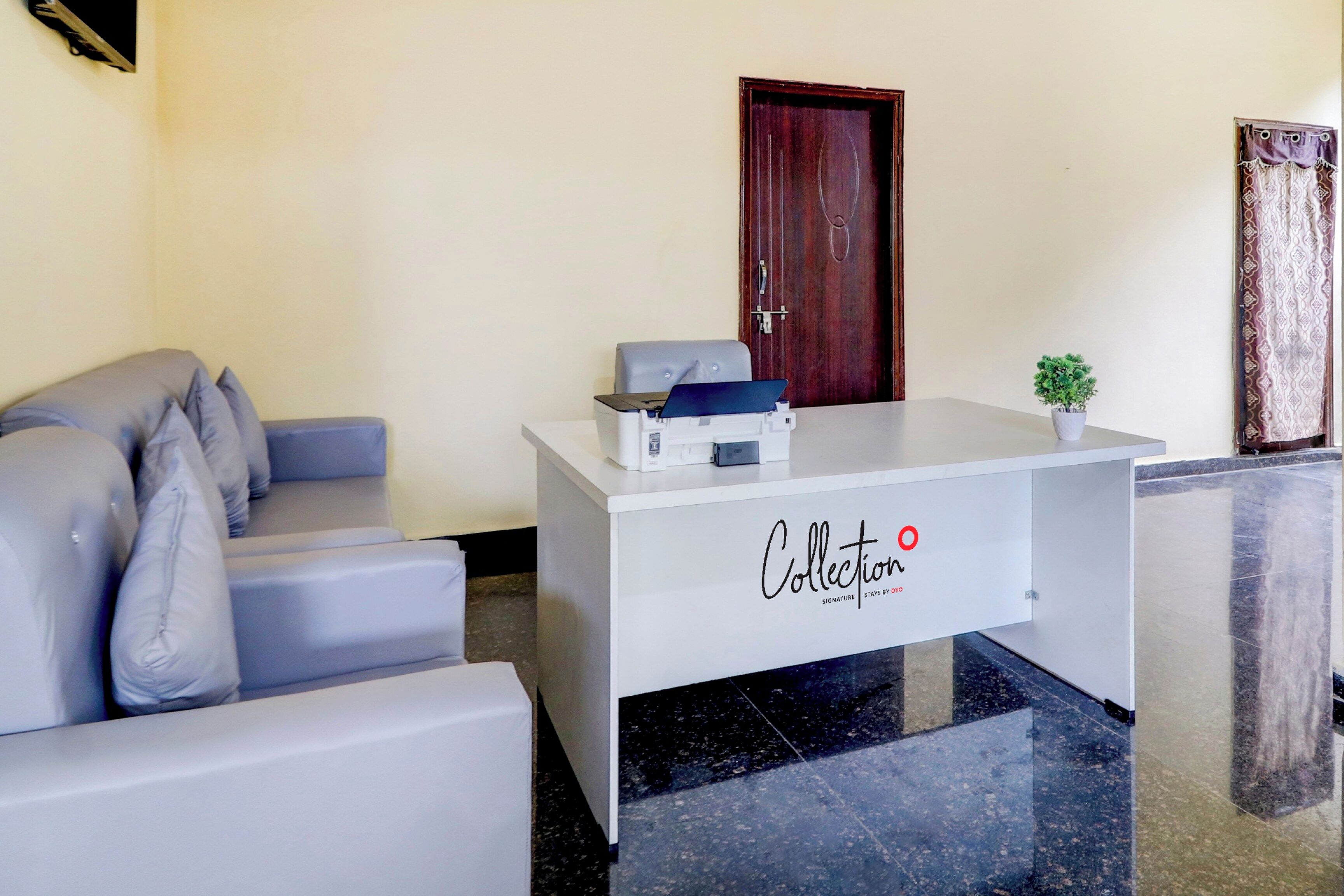 Una recepción con un logotipo, un sofá gris y una pequeña planta en maceta.