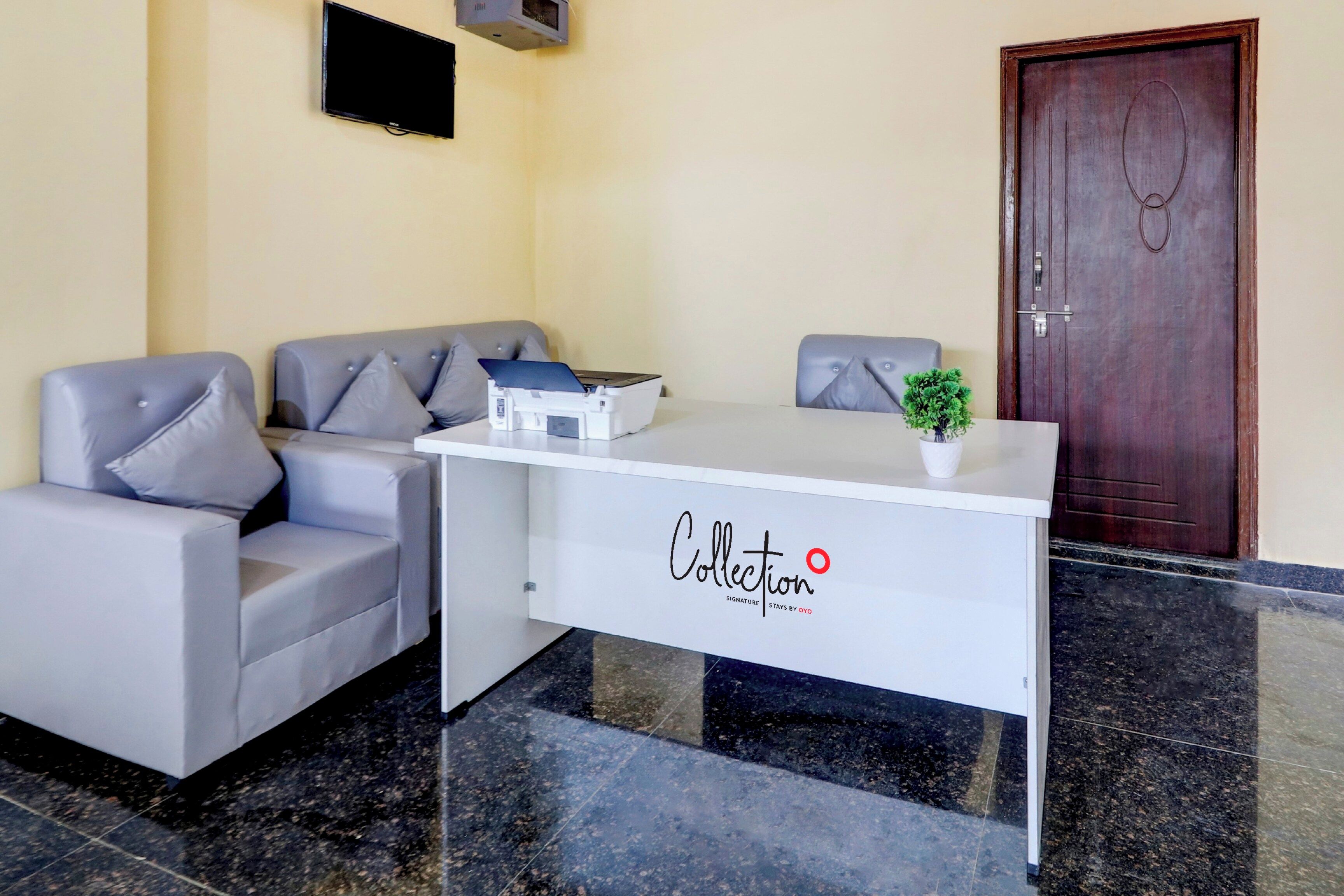 Un mostrador de recepción con un logotipo, un televisor de pantalla plana montado en la pared y una puerta de madera al fondo.