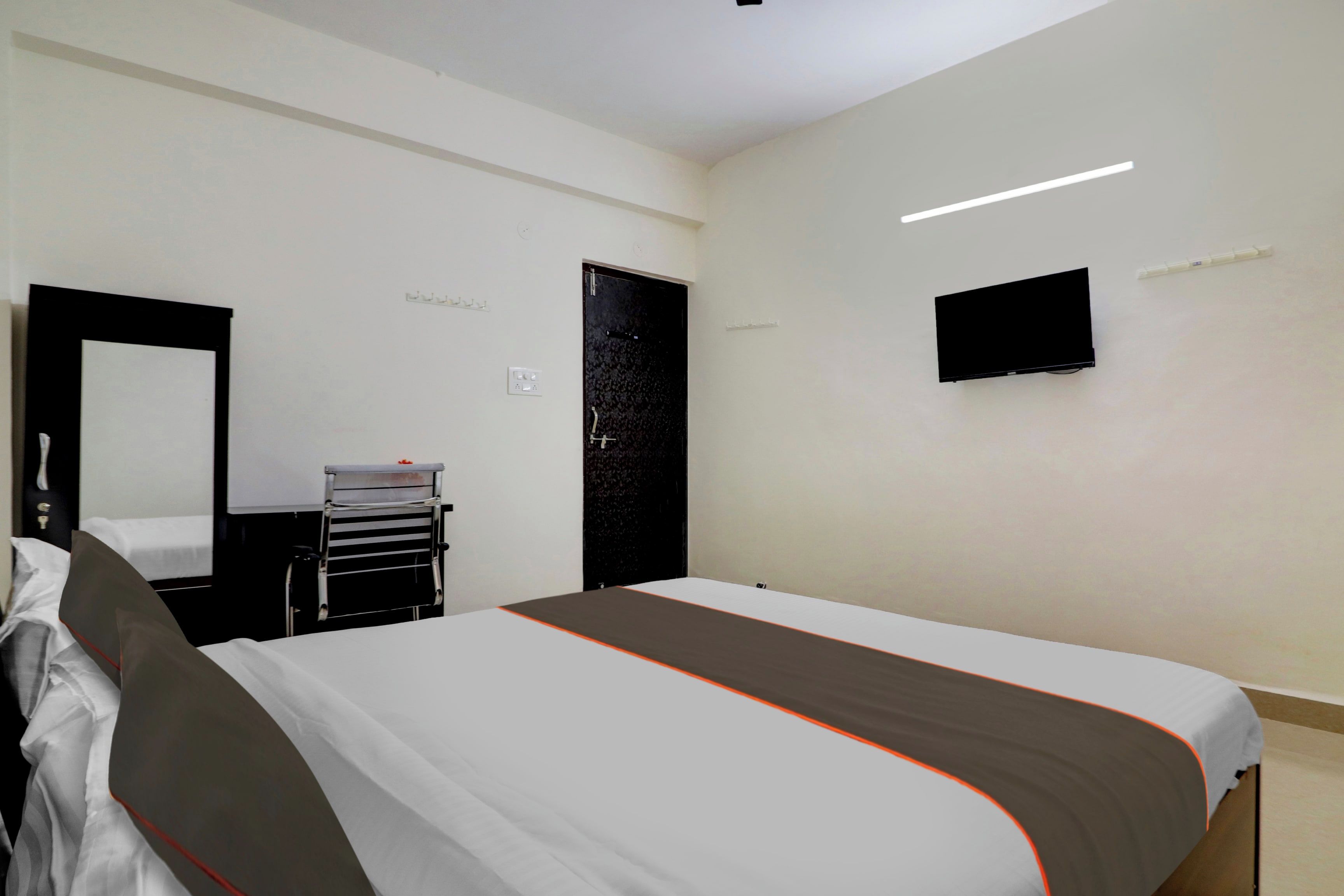 Una habitación de hotel con cama, escritorio con silla, televisor de pantalla plana montado en la pared y una puerta.