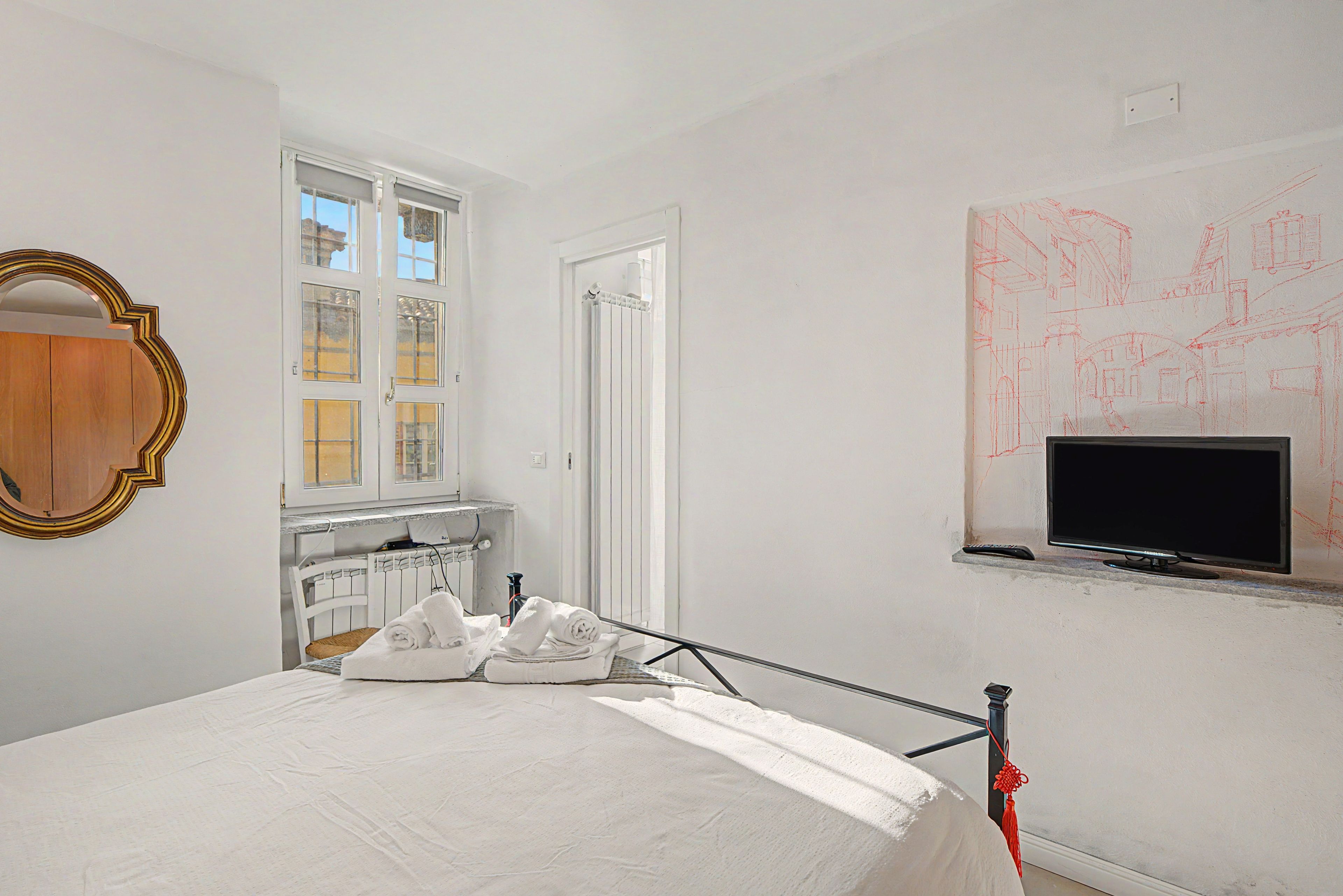 Ein Schlafzimmer mit einem Bett, einem Fenster, einem Heizkörper, einem Fernseher und einer Wand mit roten Skizzen.