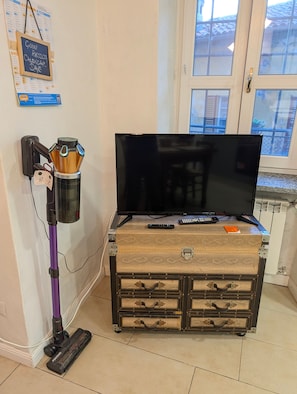 A room with a television on a vintage suitcase, a vacuum cleaner, and a wall calendar. - Holiday home 'Lake Maggiore Al Portico in Lesa' with terrace (Lesa)