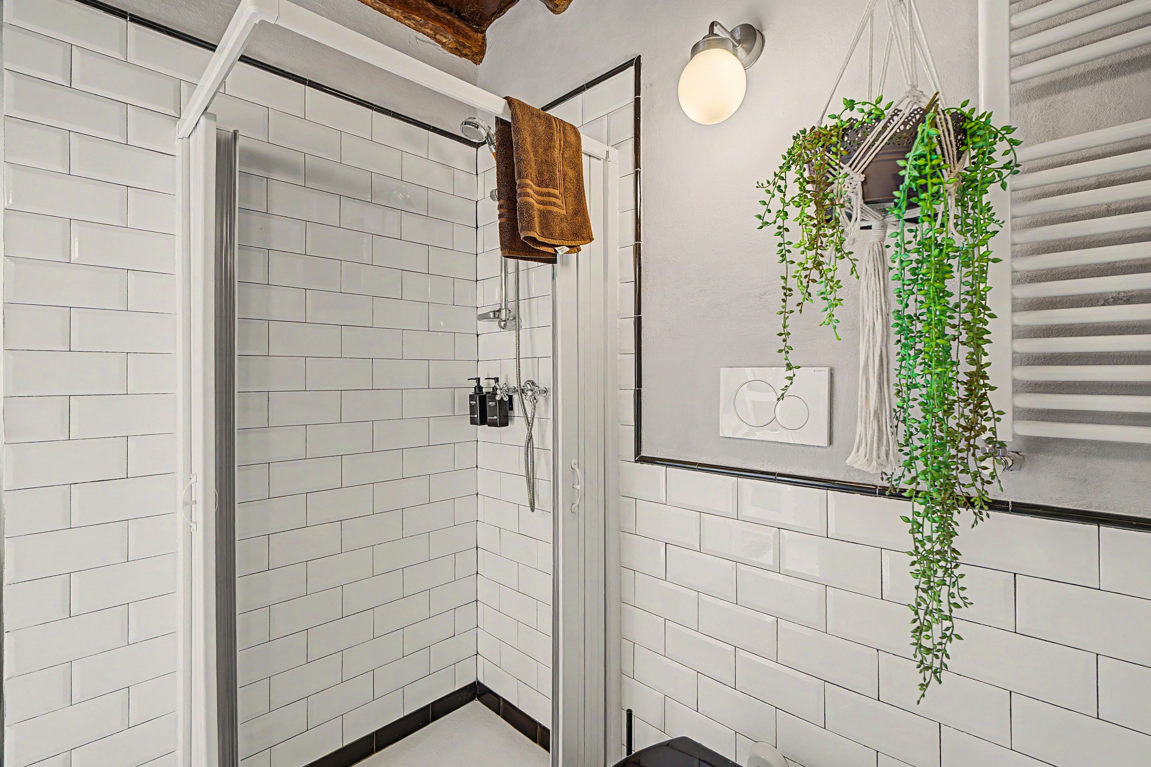 Un bagno con pareti in piastrelle bianche, box doccia in vetro e pianta pensile.