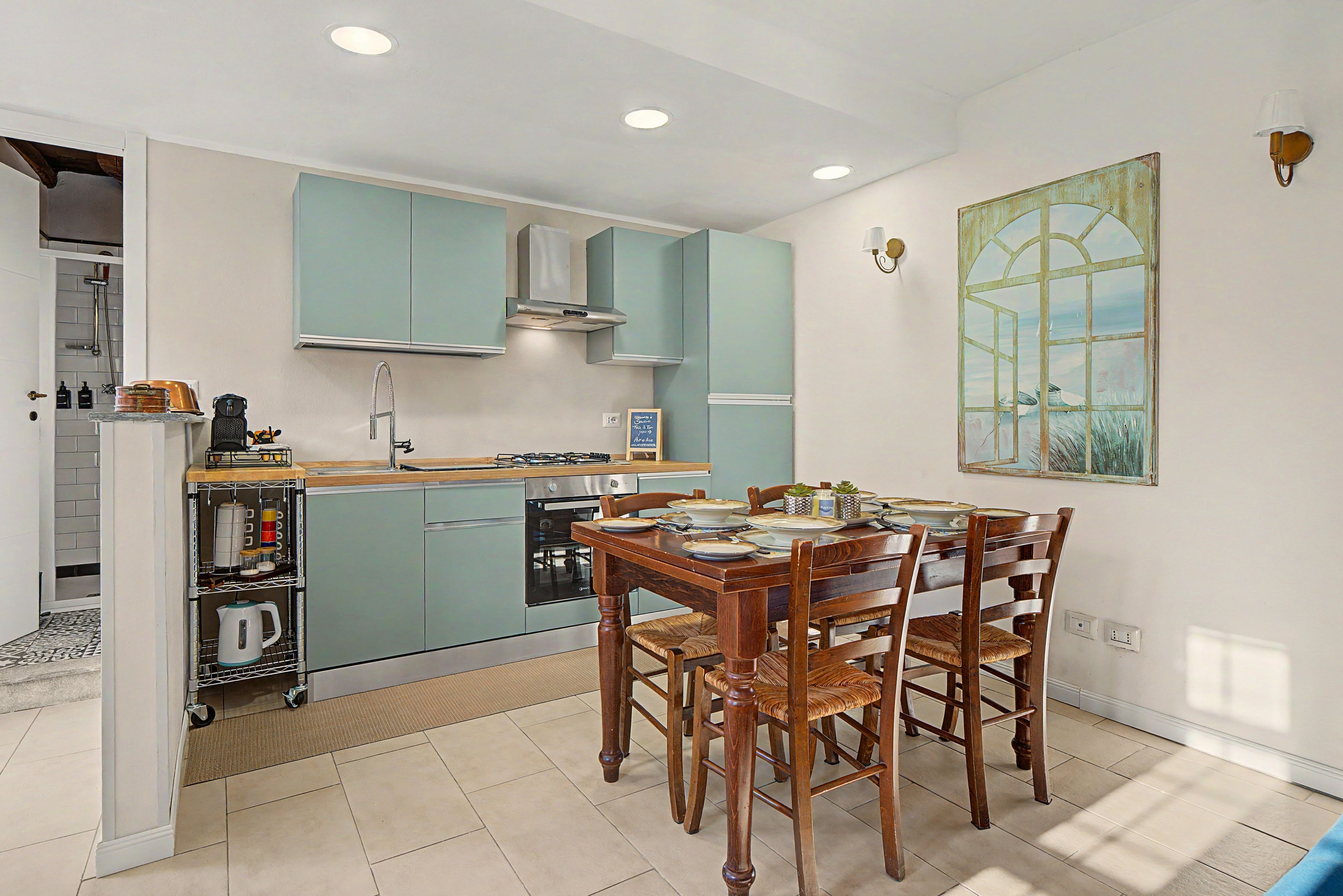 Een moderne keuken met blauwgroene kastjes, een eettafel met stoelen en een groot raam met uitzicht.