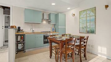 Een moderne keuken met blauwgroene kastjes, een eettafel met stoelen en een groot raam met uitzicht.