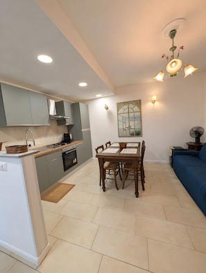 A modern kitchen with grey cabinets, a dining table with chairs, and a blue sofa in the living area. - Holiday home 'Lake Maggiore Al Portico in Lesa' with terrace (Lesa)