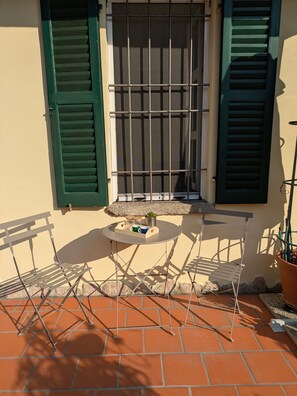 Una terrazza con tavolo, sedie e una finestra con persiane verdi.