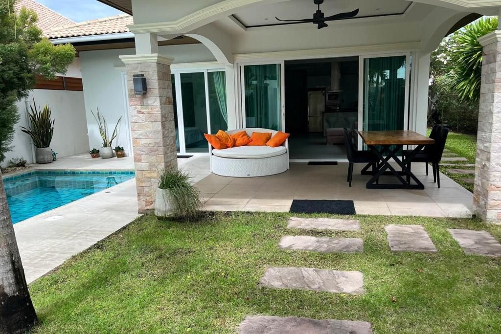 A covered outdoor seating area with a pool, stone steps, and a dining table with chairs.
