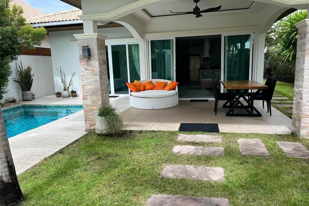 A covered outdoor seating area with a pool, stone steps, and a dining table with chairs.
