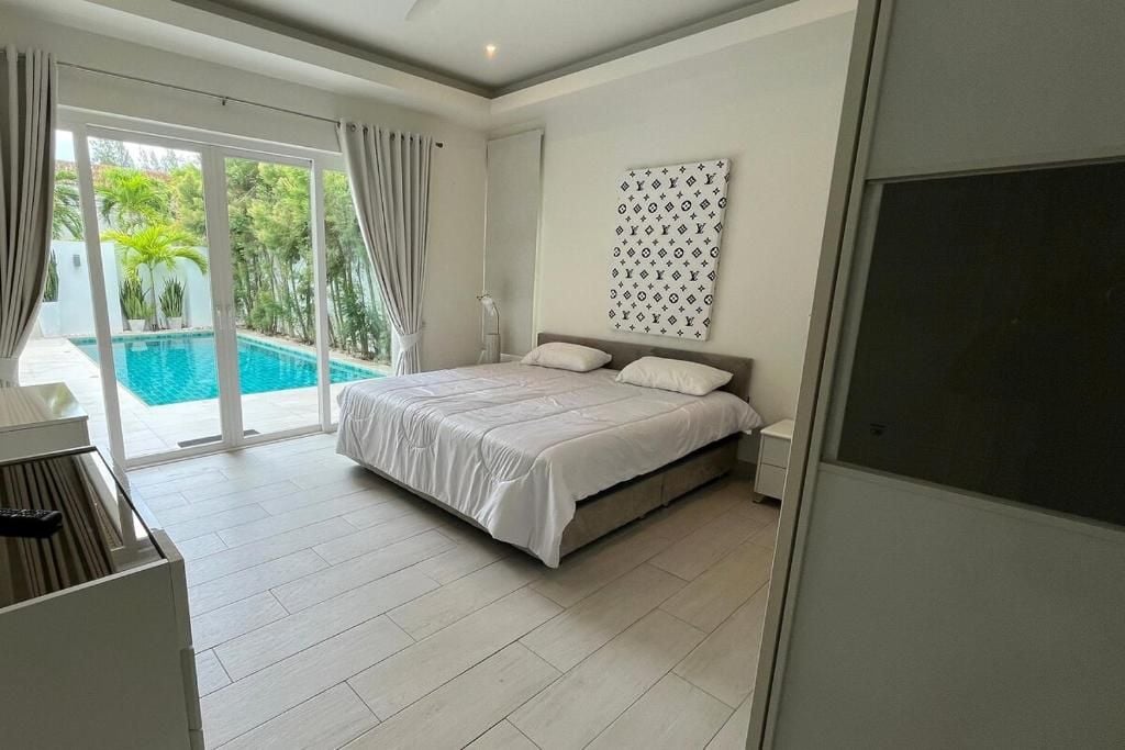 Un dormitorio con cama, ventana grande y vista a una piscina.