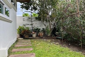 Un jardín con un sendero de piedra que lleva a un edificio blanco, rodeado de plantas en macetas y árboles.