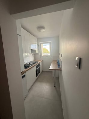 A compact kitchen with white cabinets, a stove, and a window providing natural light. - Lumina 2BR Apt w/ Balcony near Center (Warszawa)