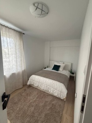 A bedroom with a bed, a nightstand, a bedside table, a window with curtains, and a ceiling light fixture. - Lumina 2BR Apt w/ Balcony near Center (Warszawa)