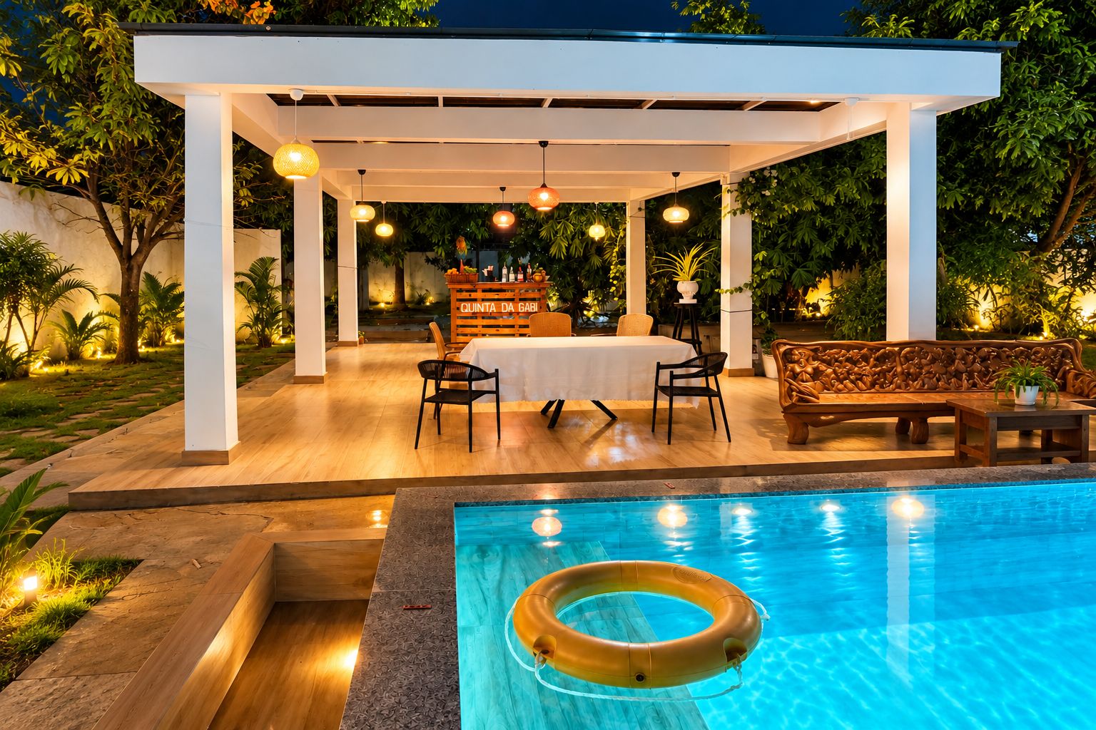 An outdoor pool area with a covered seating area, a table, and chairs.
