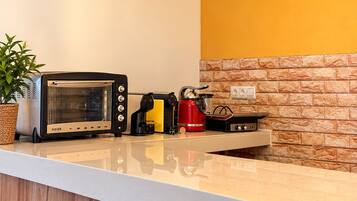 Une cuisine au design moderne, avec un plan de travail blanc, une cuisinière encastrée, une bouilloire rouge et une radio d’époque.