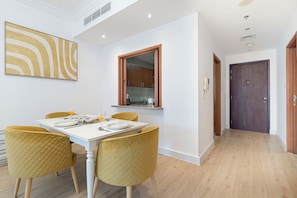 A dining area with a white table, yellow chairs, and a kitchen visible through an open door. - Sleek 1BHK , Dubai Marina (Dubai)