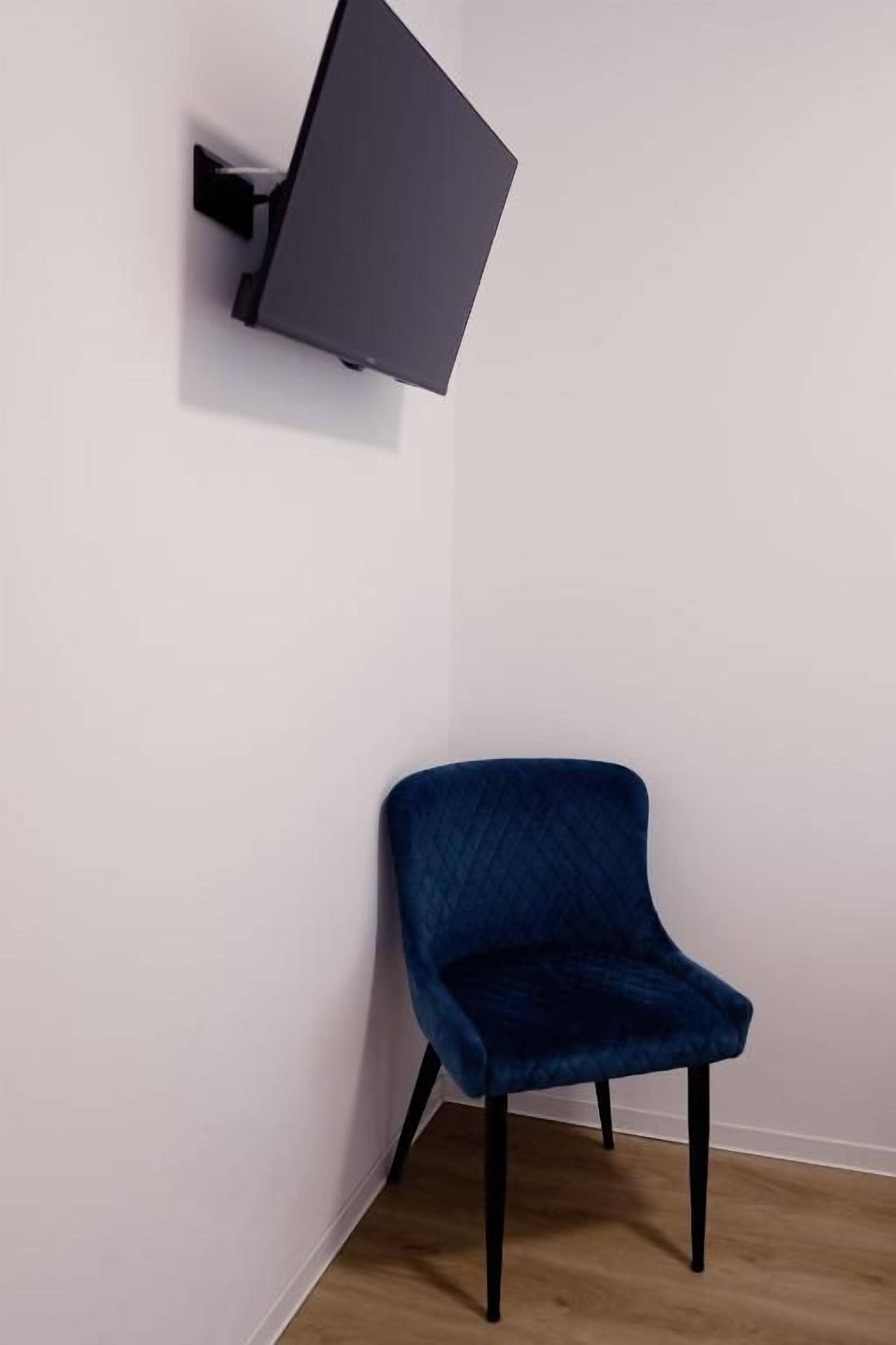 Rincón de una habitación con una silla oscura y un televisor de pantalla plana montado en la pared.