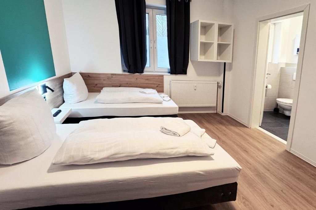 A hotel room with two beds, a window with curtains, a white radiator, and a bathroom visible through an open door.