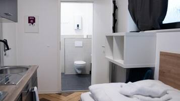A hotel room with a bed, a small kitchenette, a bathroom with a toilet and sink, and a TV mounted on the wall.