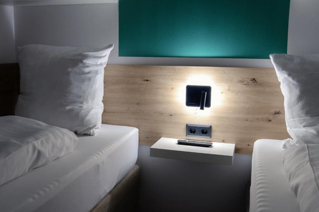 Ein Hotelzimmer mit einem hölzernen Kopfteil, einem Nachttisch mit Fernbedienung und einer grünen Wand.
