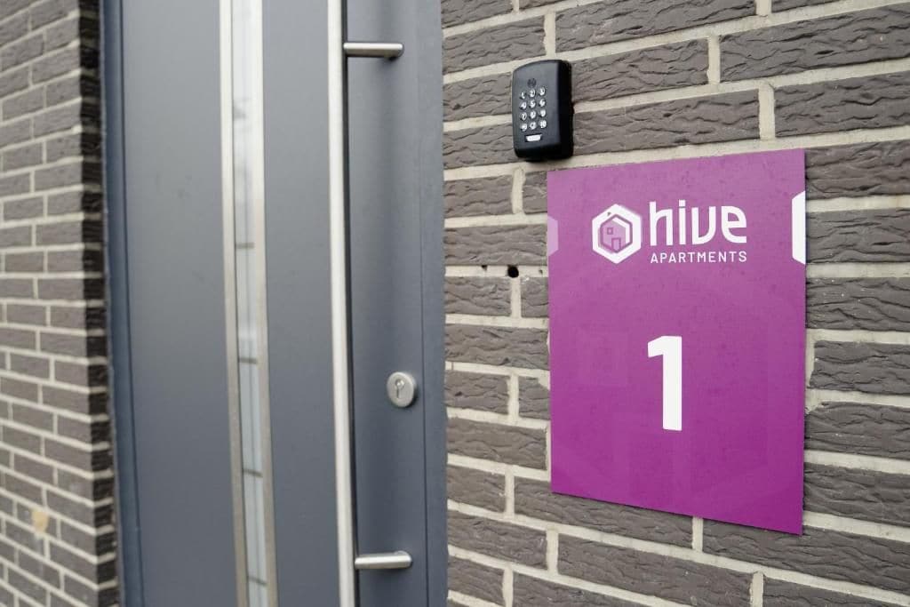 A door with a keypad lock and a purple apartment sign indicating 'hive apartments' and the number '1'.