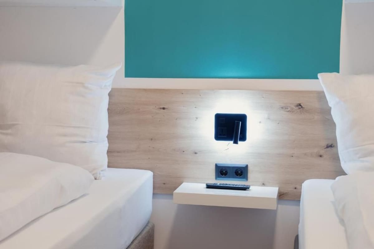 Ein Schlafzimmer mit zwei Betten, einem Nachttisch mit Fernbedienung und einer türkis farbenen Wand.