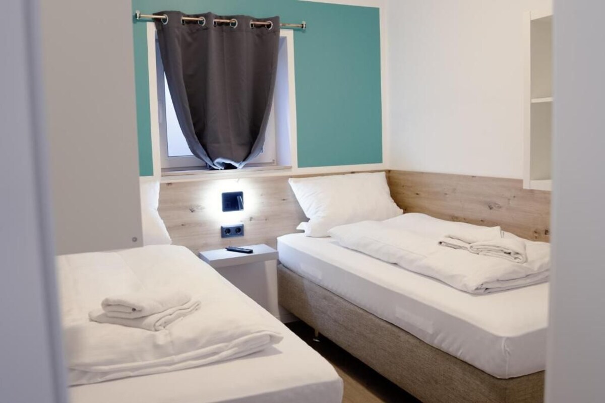 Ein Hotelzimmer mit zwei Betten, einem Fenster mit Vorhängen, einem Nachttisch und einem Beistelltisch.