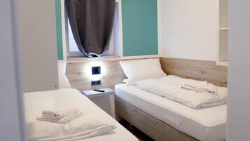 A hotel room with two beds, a window with curtains, a bedside table, and a nightstand.