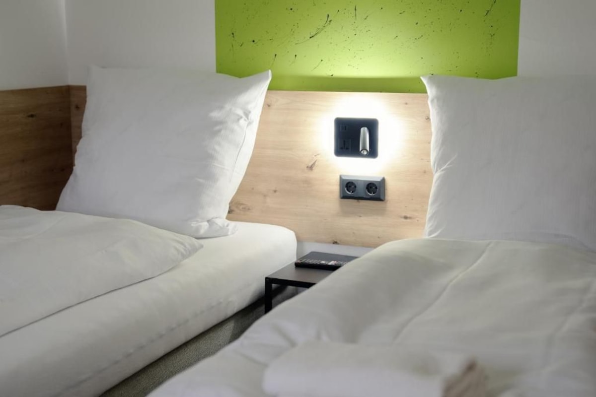 Ein Bett mit weißer Bettwäsche, ein Nachttisch mit Fernbedienung und eine Wandleuchte.
