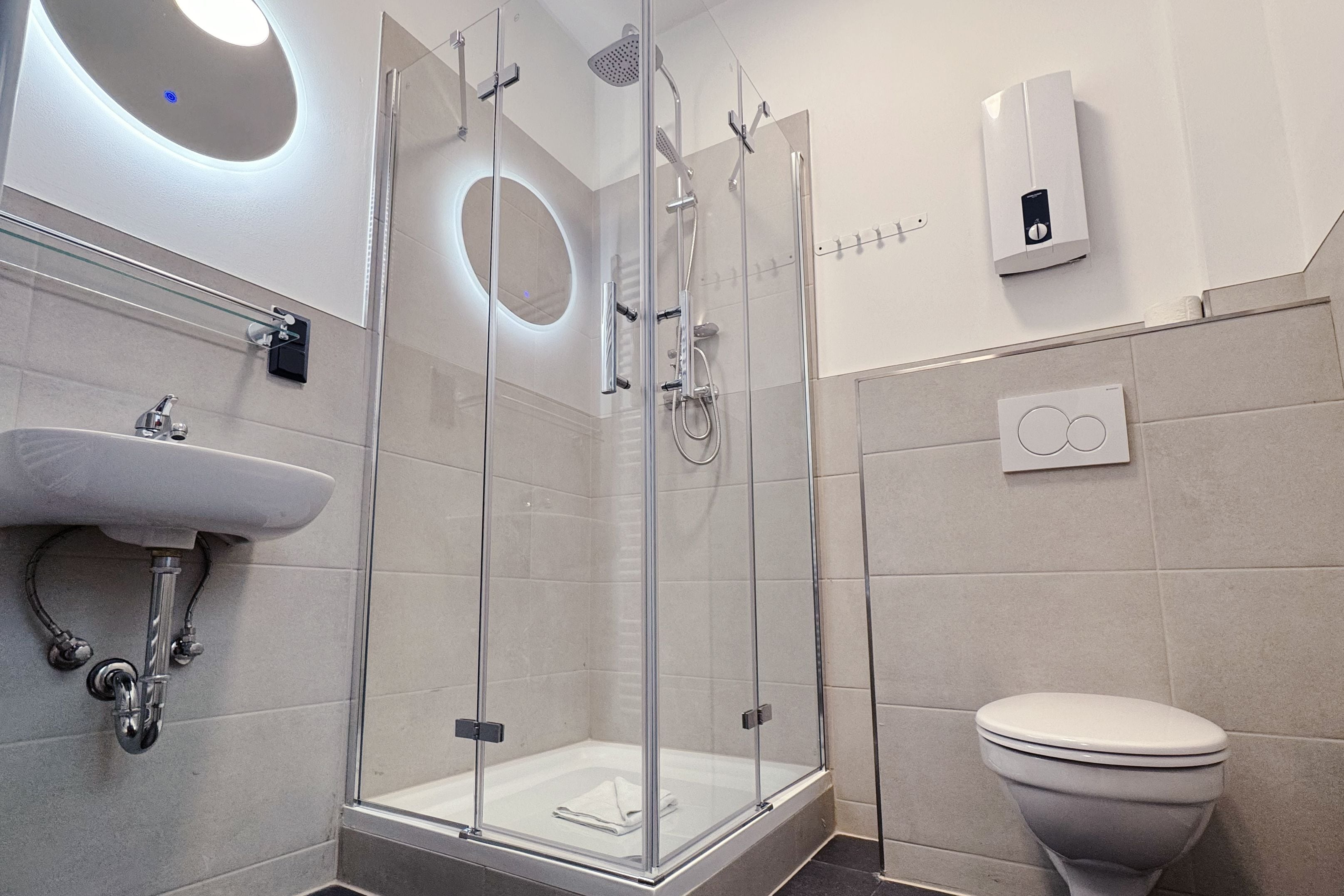Ein modernes Badezimmer mit einer gläsernen Dusche, einem weißen Waschbecken und einer Toilette.