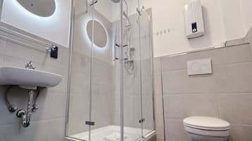 Ein modernes Badezimmer mit einer gläsernen Dusche, einem weißen Waschbecken und einer Toilette.
