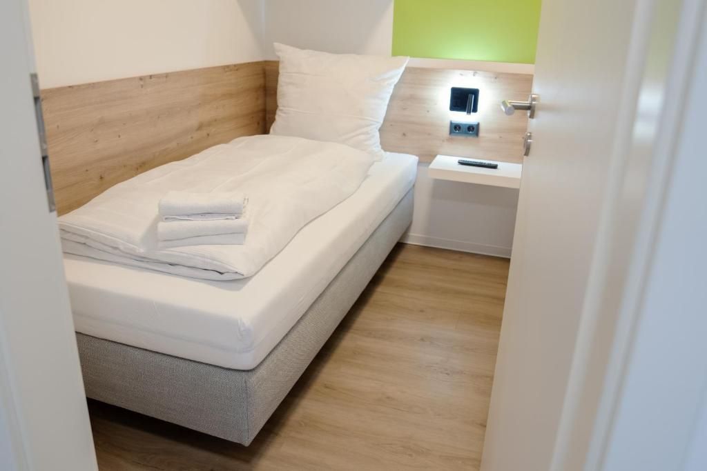 A neatly made bed with white linens, a bedside table with a remote control, and a wooden headboard.